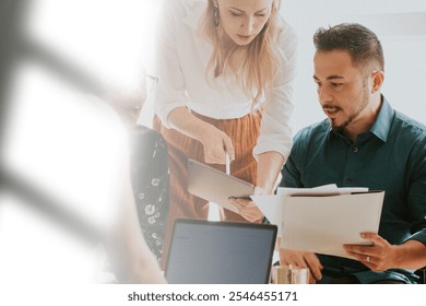 Two colleagues collaborating, reviewing business documents. Office teamwork, diverse business professionals. Focused discussion meeting in a modern office setting. Diverse business meeting concept. - Powered by Shutterstock