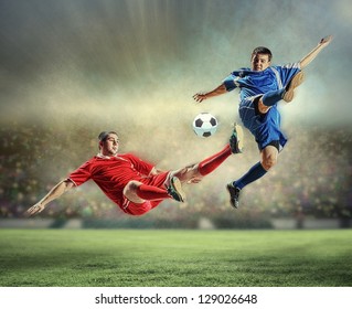 two football players in jump to strike the ball at the stadium - Powered by Shutterstock