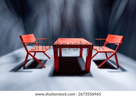 Two red chairs and table in spotlight in empty dark interrogation room.