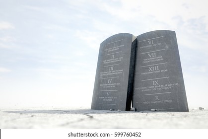 Two stone tablets with the ten commandments inscribed on them standing in brown desert sand infront of a blue sky - 3D render