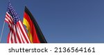 US and German flags on flagpoles on the side. Flags on a blue background. Place for text. United States of America. Berlin, Europe. Commonwealth. 3D illustration.