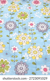 A vibrant and playful textile pattern featuring stylized flowers in pink, yellow, green, and gray. The design is set against a soft light blue background with vertical vine details. Perfect for nursery decor, children's clothing backgrounds, stationery design, summer-themed marketing, and cheerful website backdrops.