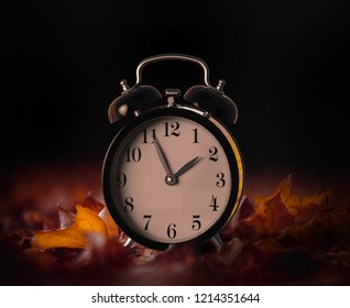 Vintage alarm clock buried underneath colorful fallen autumn leaves with shallow depth of field. Daylight savings time concept with clock hands at almost 2 am, 3D illustration - Powered by Shutterstock