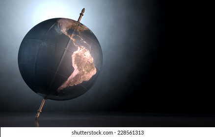 A vintage world globe tilted and standing on a central axis on an isolated spotlit dark background