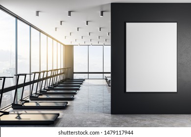 White Blank Poster On Black Wall In Modern Gym With Light Interior, Concrete Floor And Benches, Black Treadmills And Big Windows With City View From Skyscraper. 3D Rendering