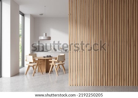 White kitchen interior with dining table on grey concrete floor. Modern kitchenware on deck. Panoramic window on tropics. Empty wooden copy space partition. 3D rendering
