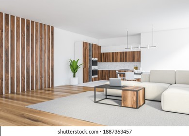 White Living Room With White Sofa And Wooden Coffee Table With Laptop, Eating Table And Chairs, Side View. Wooden Kitchen Set With Shelves On Background, 3D Rendering No People