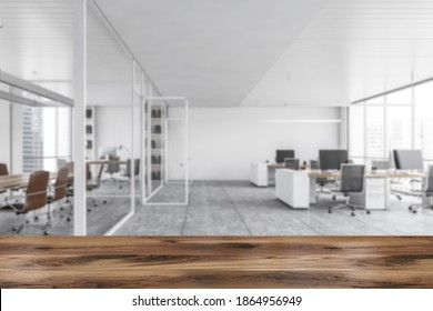 White Office Open Space Room, Wooden Desk On Foreground. Blurred Background With Tables And Computers, Conference Room With Chairs And Tables Behind Glass Doors. 3D Rendering, No People