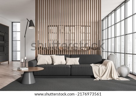 White studio interior with sofa on carpet and coffee table with decoration. Cooking area with kitchen appliances behind partition, hardwood floor. Panoramic window on city view. 3D rendering