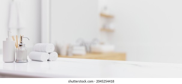 White Table Top Or Counter Top With Shampoo Bottles, Hand Towels, Toiletries Over Blurred Modern Bright White Bathroom Interior. 3d Rendering, 3d Illustration