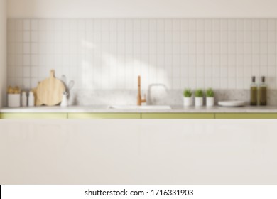 White Table For Your Product Standing In Blurry Kitchen With White Tiled Walls And Green Countertops With Built In Sink. 3d Rendering Mock Up