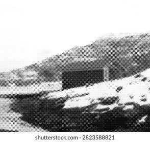 A winter mountain landscape with a dark rectangular cabin near a snow-covered slope, rugged hills rising behind it, and dark water or shoreline in the foreground, reconstructed with large black halftone dots and strong graphic contrast.