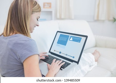 Woman sitting on sofa and checking her social media profile on the laptop - Powered by Shutterstock