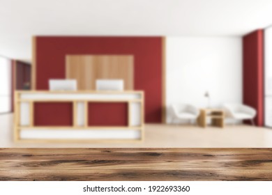 Wooden desk foreground on blurred background of red and wooden reception room, armchairs with coffee table near window. Office entrance room with furniture, 3D rendering no people