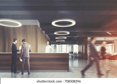 Wooden Reception Desk Is Standing In A Modern Office With A Concrete Floor, Light Wooden Walls, Round Ceiling Lamps And Armchairs. People. 3d Rendering Mock Up Toned Image