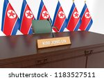 Wooden table with desk plate KIM JONG UN and national flags behind. 3D Illustration.