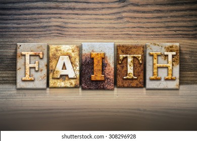 The word "FAITH" written in rusty metal letterpress type sitting on a wooden ledge background.