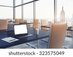 Workplaces in a modern corner panoramic office in New York. Black tables and brown leather chairs. A laptop with a white screen, notepad and a coffee cup. 3D rendering. Toned image.