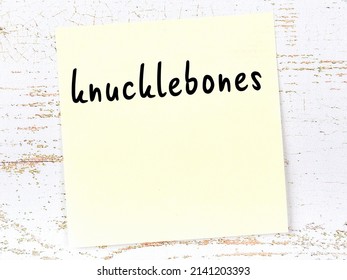 Yellow sticky note on wooden wall with handwritten inscription knucklebones