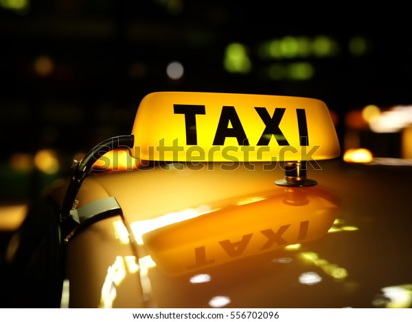Yellow taxi sign at night. Taxi\
car on the street at night. Taxi car roof sign on bokeh\
background