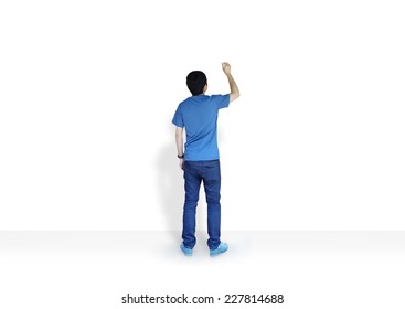 Young Man Writing Something On White Wall Background.