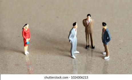 One miniature woman standing apart from a group of three miniature men.