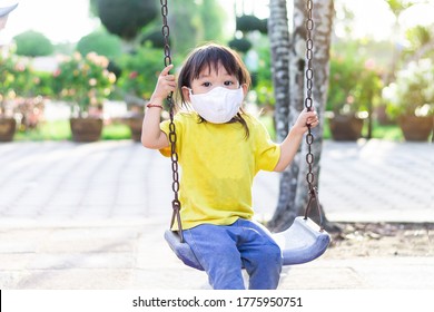 Happy​ Asian​ Child​ Girl​ Wearing​ A​ Fabric​ Face​ Mask​ When​ She​ Playing​ A​ Toy​ At​ The​ Playground.​ Social​ Distance.​ 