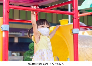 Happy​ Asian​ Child​ Girl​ Wearing​ A​ Fabric​ Face​ Mask​ When​ She​ Playing​ A​ Toy​ At​ The​ Playground.​ Social​ Distance.​ 