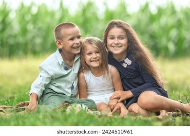 Трое детей сидят на траве и смеются. Брат и две сестры смеются, сидя на земле. Дети на природе, на траве обнимаются и смеются.