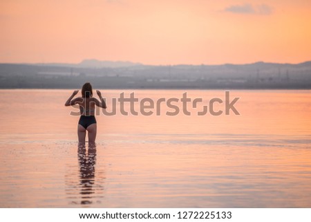 Девушка идет по воде на закате. Вид сзади. Горизонтальный формат.