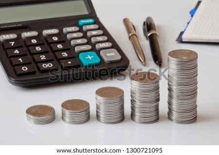 Coin columns, calculator, notepad and pen on a white table