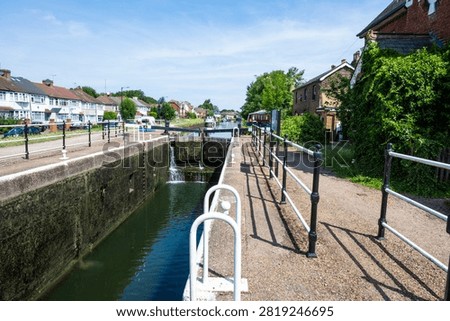 Photo of Enfield Lock on the River Lea Navigation in north London, showing lock gates, towpath, and riverside houses on a sunny day.