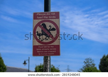 Close‑up of a public sign at Enfield Island Village reading “Please do not feed the birds,” warning that food attracts vermin and poses health risks.