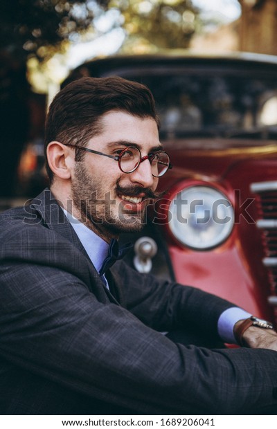 01.06.2019 Tbilisi, Georgia:\
portrait of a stylish young Georgian man with mustache and vintage\
tuxedo posing for a photo on the background of the old city in\
Tbilisi