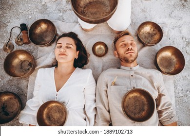 01.06.2019 Vinnitsa, Ukraine: group therapy with Tibetan singing bowls for a girl and a boy lying on the ground in the middle of the desert surrounded by copper bowls, meditation and relaxation