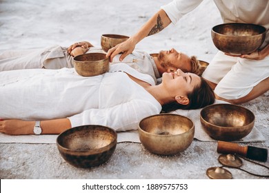 01.06.2019 Vinnitsa, Ukraine: group therapy with Tibetan singing bowls for a girl and a boy lying on the ground in the middle of the desert surrounded by copper bowls, meditation and relaxation