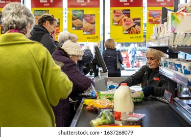 02/05/2020 Chichester, West Sussex, UK A Supermarket Cashier Scanning Items At The Checkout Taking Items From The Conveyor Belt That Has Products On