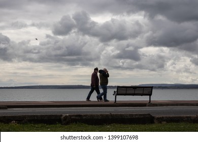 04/09/2019 Portsmouth, Hampshire, UK A Middle Aged Couple Walking Their Dog Along The Beach On A Windy And Stormy Day 