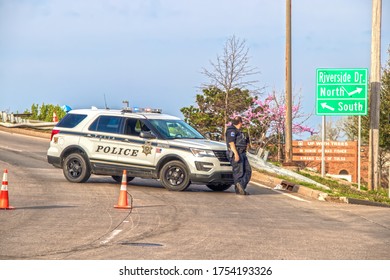 04_06_2019 Tulsa USA - Tulsa Cop Leans On Front Of His Police Car Blocking Overpass With Orange Cones On Overcast Day With Damaged Railing Behind And Redwood Tree In Bloom