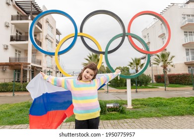 05,04,2021 Russia, Sochi One Person Little Funny Happynes Girl Stands With The Flag Of Russia Next To The Olympic Rings The Theme Of The Olympic Games