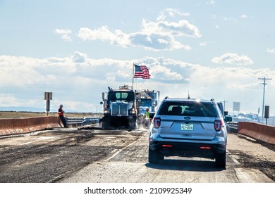 05-20-2021 - New Mexico USA - Traffic Delay With Road Construction With Workers And Trucks With Huge American Flag And Dust And Texas Car In Foreground Waiting