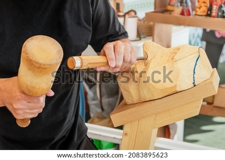 06 July 2021, Ufa, Russia: Craftsman artist and carpenter cutting wooden figure face with chisel and hammer
