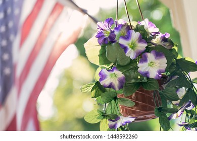 07/2019 The American Flag Flying Behind Some Hanging Potted Flowers In Stockton, CA