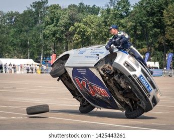 08/06/2019 Russia, Moscow. The Police Officer Shows Vocational Training Of Stuntmen Standing Outside Of The Car Going On Two Side Wheels. Replacement 
Tire Fitting Of A Front Wheel On The Run