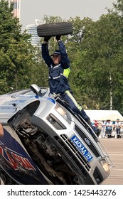 08/06/2019 Russia, Moscow. The Police Officer Shows Vocational Training Of Stuntmen Standing Outside Of The Car Going On Two Side Wheels. Replacement 
Tire Fitting Of A Front Wheel On The Run