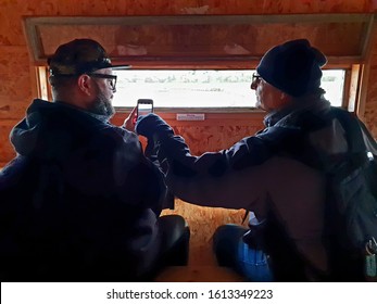 08/09/2019 Titchfield, Hampshire, UK Two Bird Watchers In A Bird Watching Hide Checking Their Sightings On A Mobile Phone Or Cell Phone  