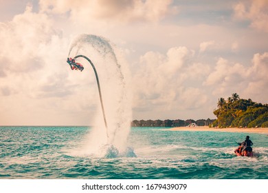 08.17.2019 - Noonu Atoll, Maldives Island Sunset. Professional Fly Board Rider Doing Back Flip With Tropical Resort Island Background. Sunset Sport And Summer Activity Background, Fun Water Sport