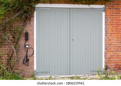 08/30/2020 Hambledon, Hampshire, UK A Set Or Garage Doors With An Electric Charging Point On The Wall To Charge An Electric Car