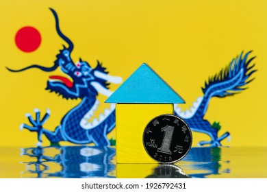 1 Chinese Yuan Coin And A Symbolic Wooden House Against The Background Of The Ancient Flag Of The Chinese Empire With A Blue Dragon On A Yellow Background