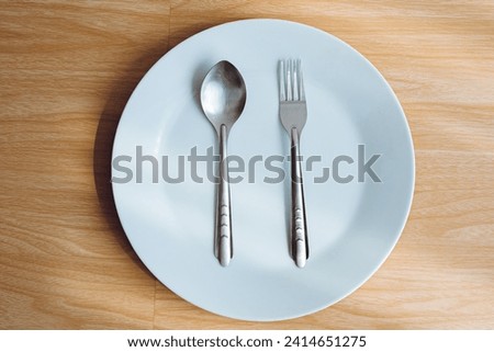 1 empty white plate and 1 pair of cutlery with a wooden background.